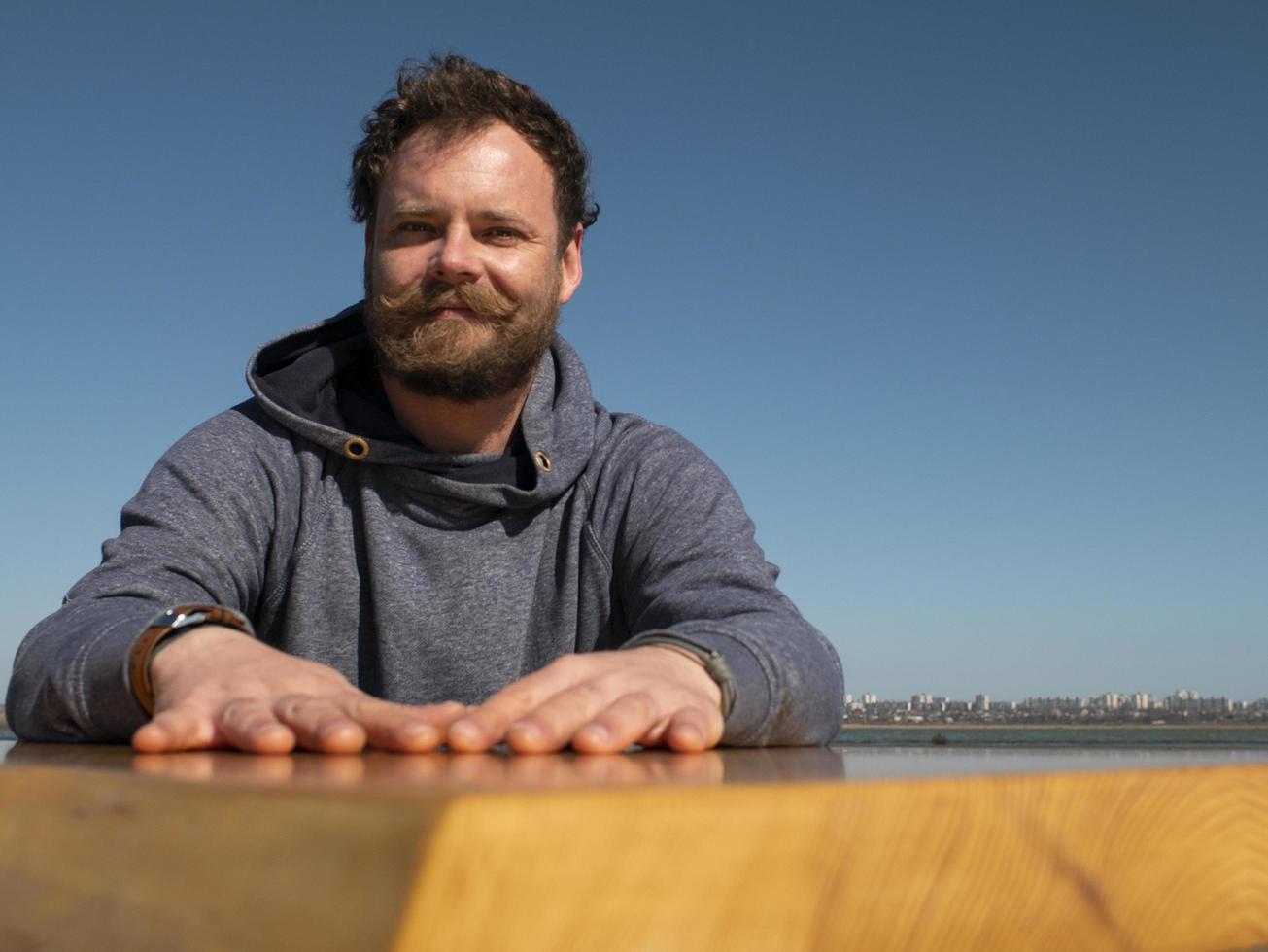 Hombre divertido con barba y bigote sentado en una mesa de café foto