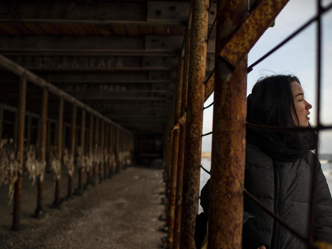 young girl in a coat stands near metal rusty structures photo