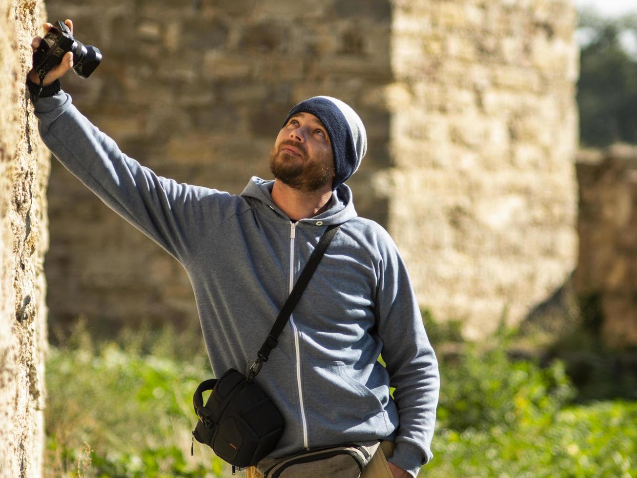 bearded man wearing a knitted hat stands against a wall photo