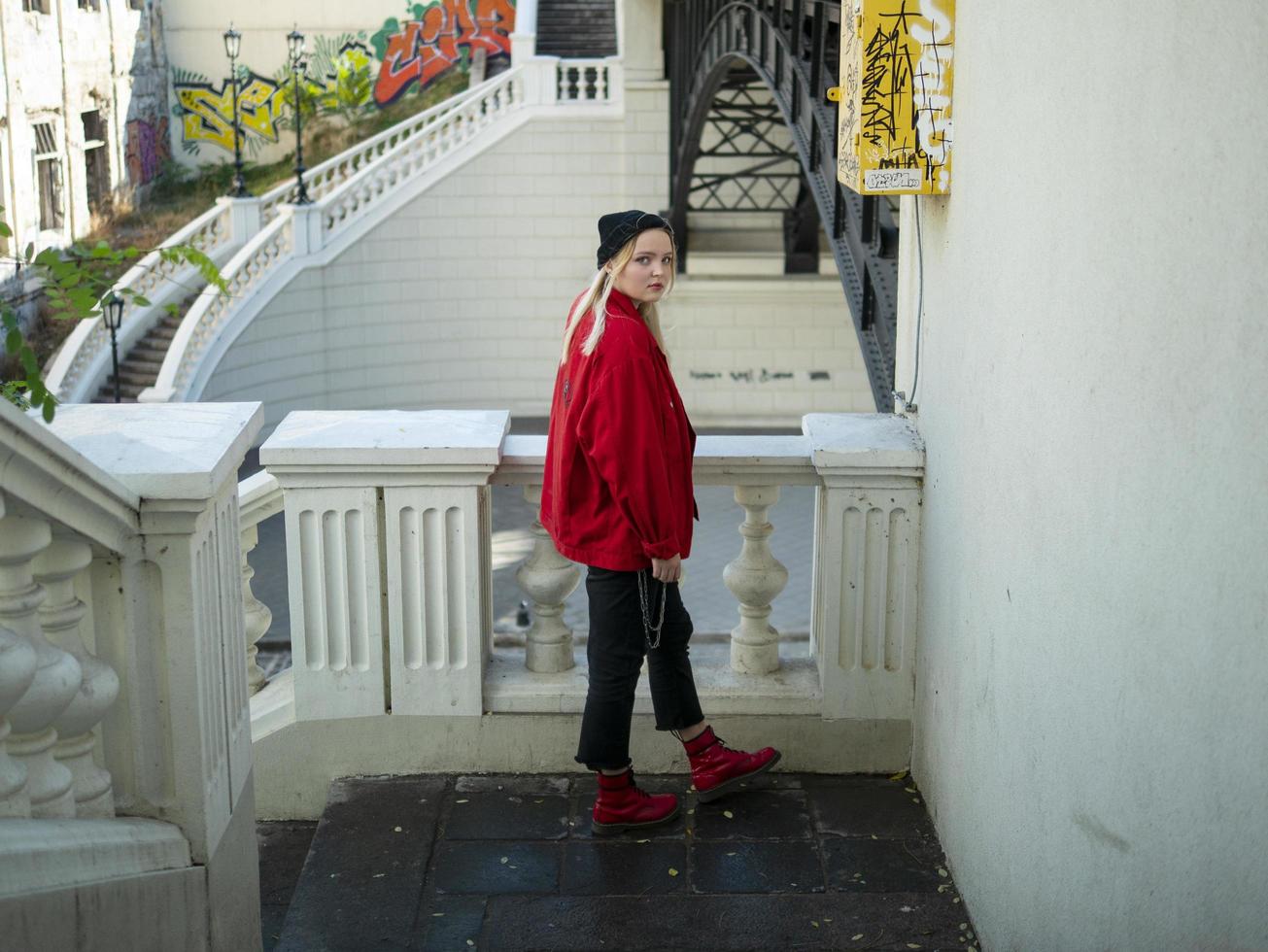 hipster girl in a red jacket is standing on the stairs photo