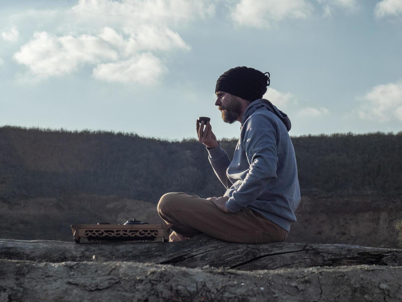 hipster man with a beard and in a knitted hat drinks tea from a bowl photo