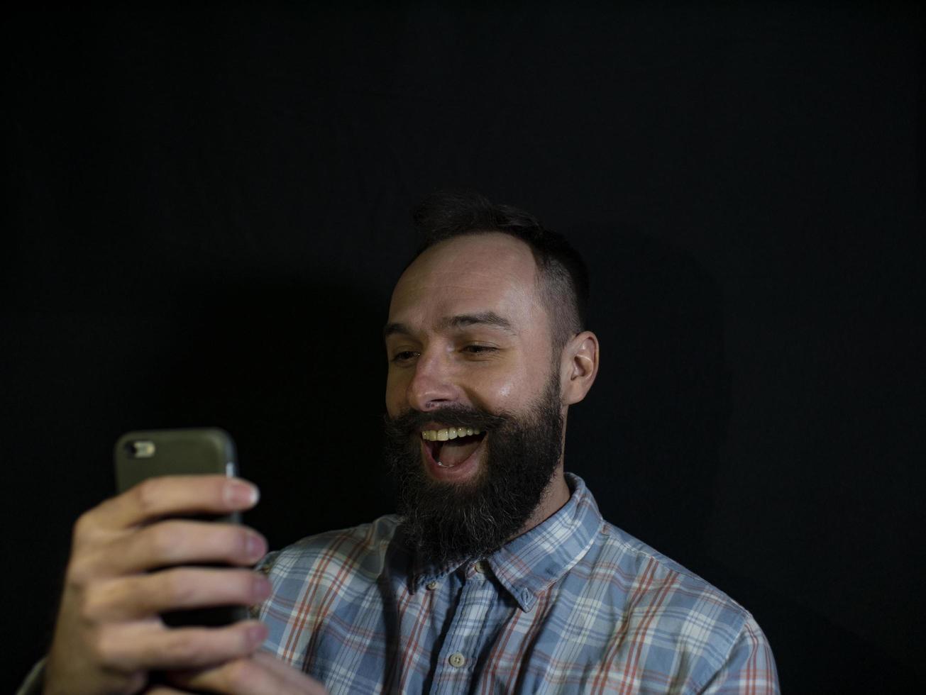 Hombre elegante con barba y bigote se ve en un teléfono móvil foto