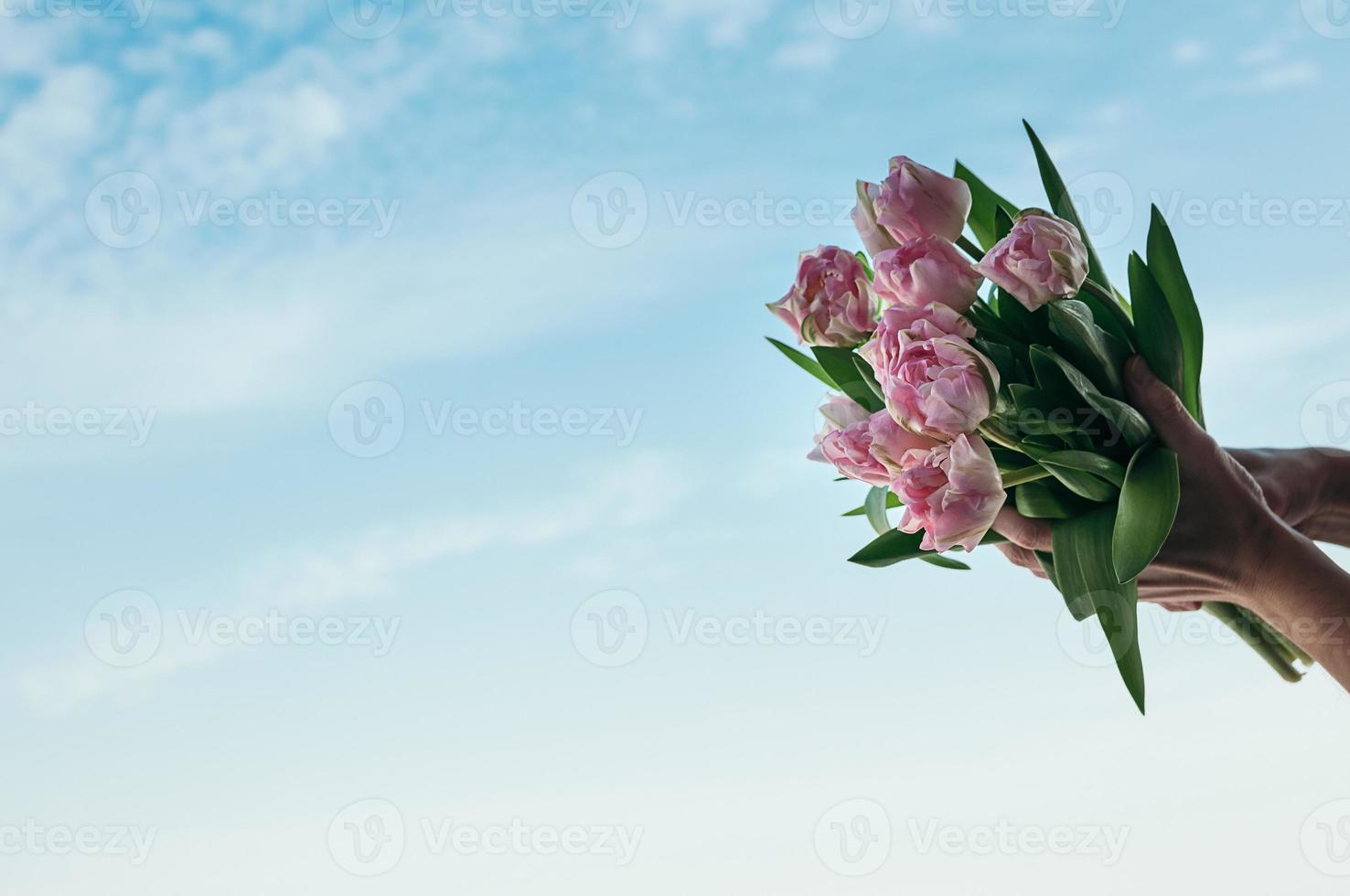 A bouquet of pink flowers in a hand against blue sky background photo