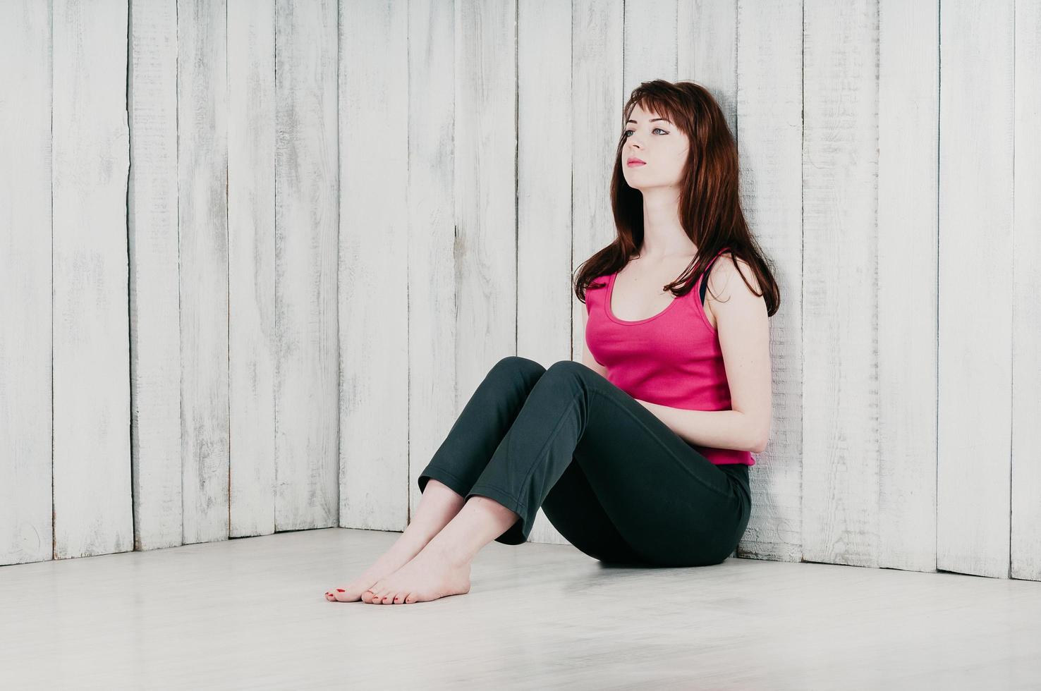a pretty girl in a pink top, sitting on the floor, leaning on wall photo