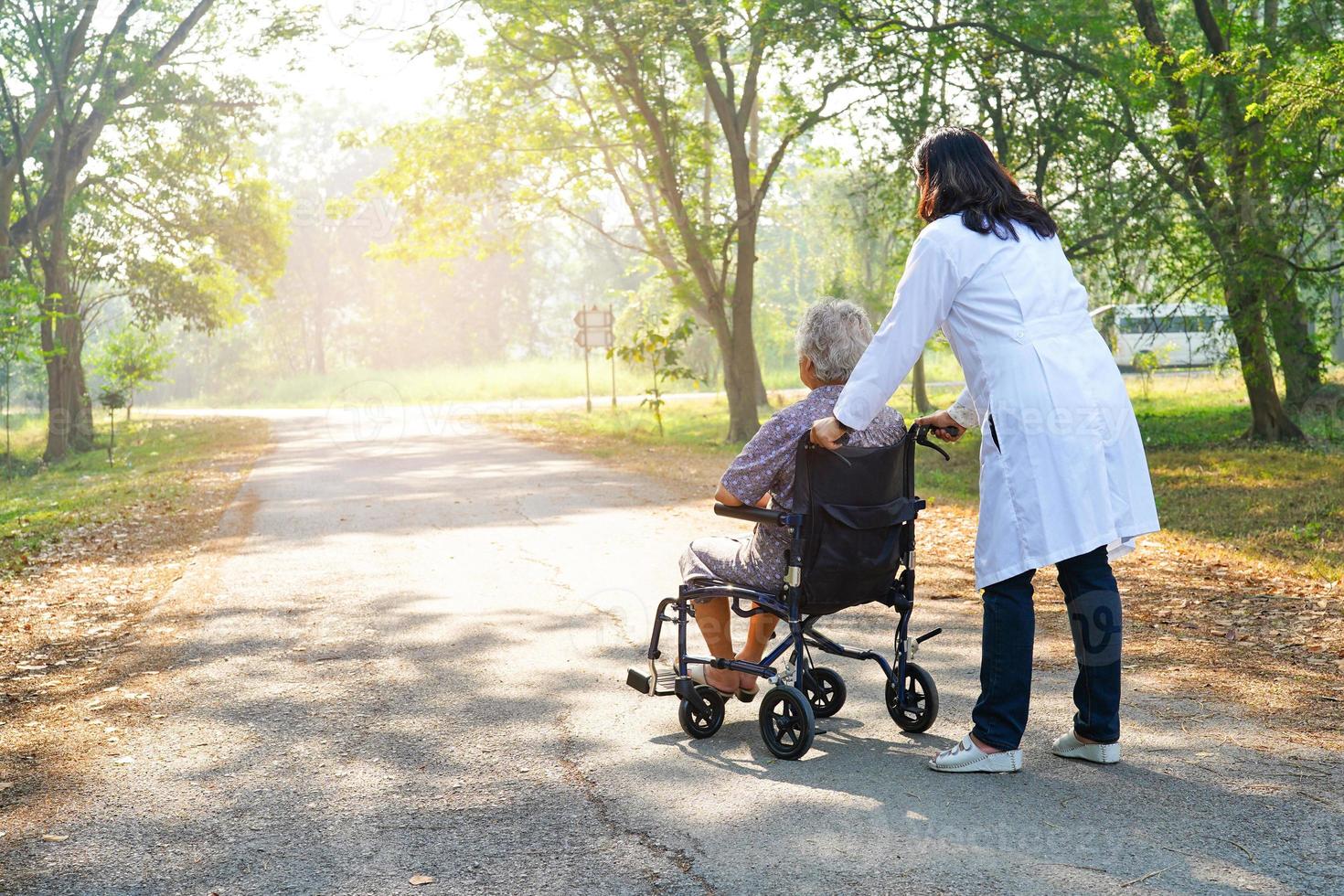 ayudar y apoyar a la paciente asiática sentada en silla de ruedas en el parque. foto