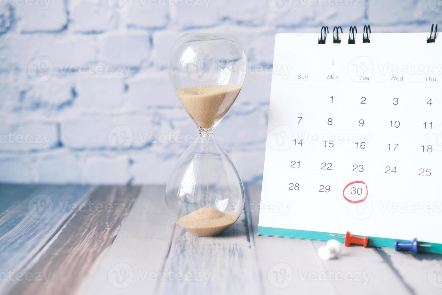 hourglass flowing through the bulb of sandglass and calendar on table photo