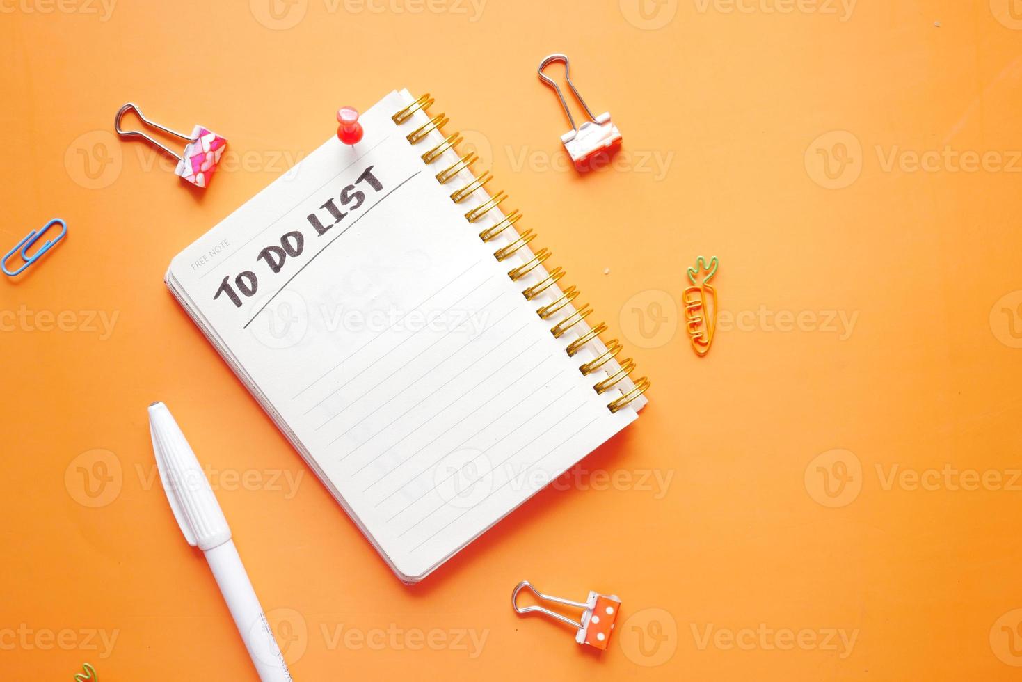 lista de tareas pendientes en el cuaderno con proveedores de oficina sobre fondo naranja. foto