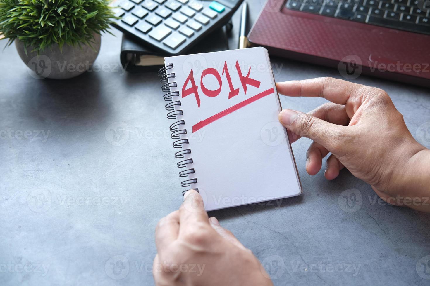 Asimiento de la mano el bloc de notas con la palabra 401k y un portátil en la mesa foto