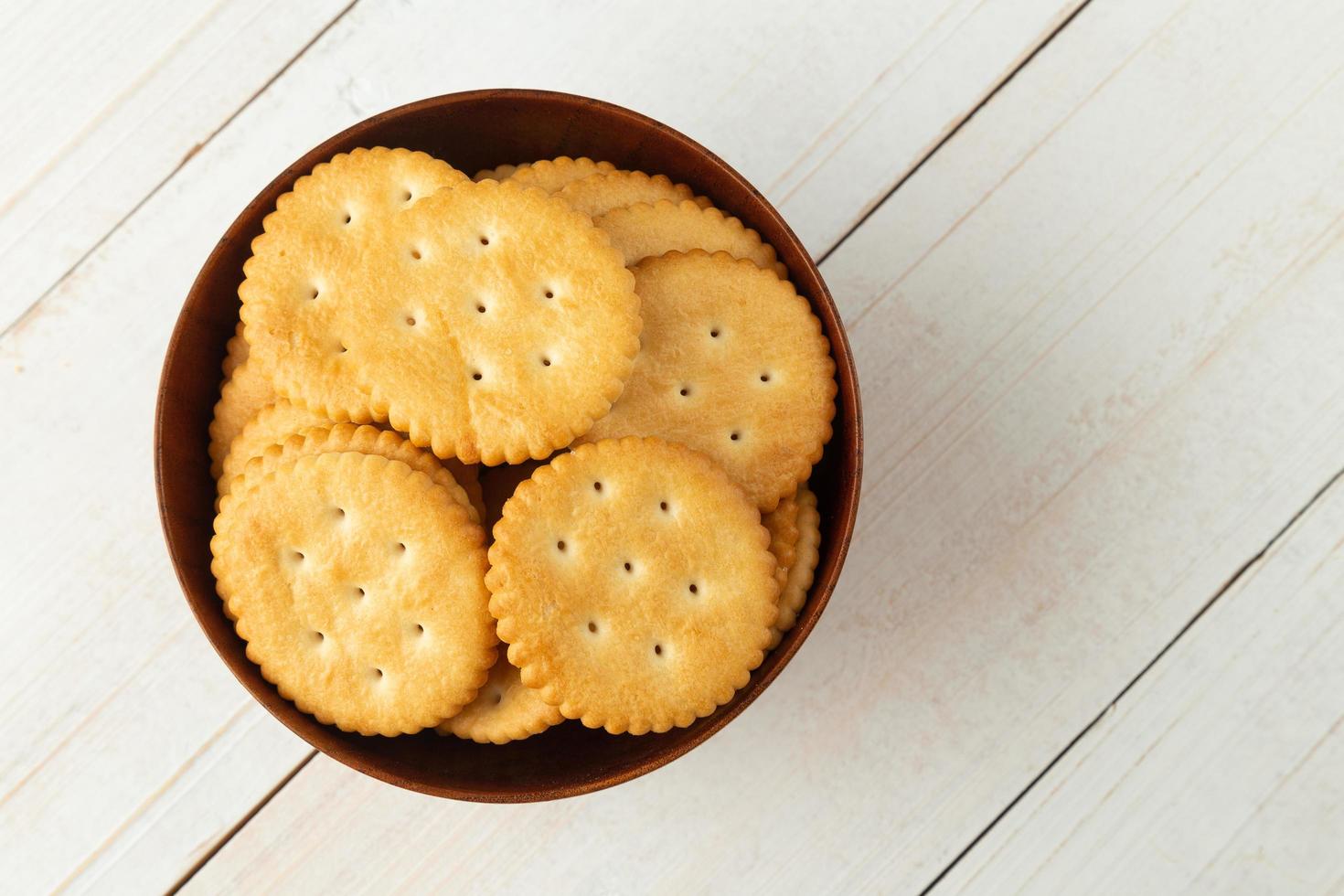 Galletas cracker redondeadas en un recipiente de madera sobre la mesa de madera blanca foto