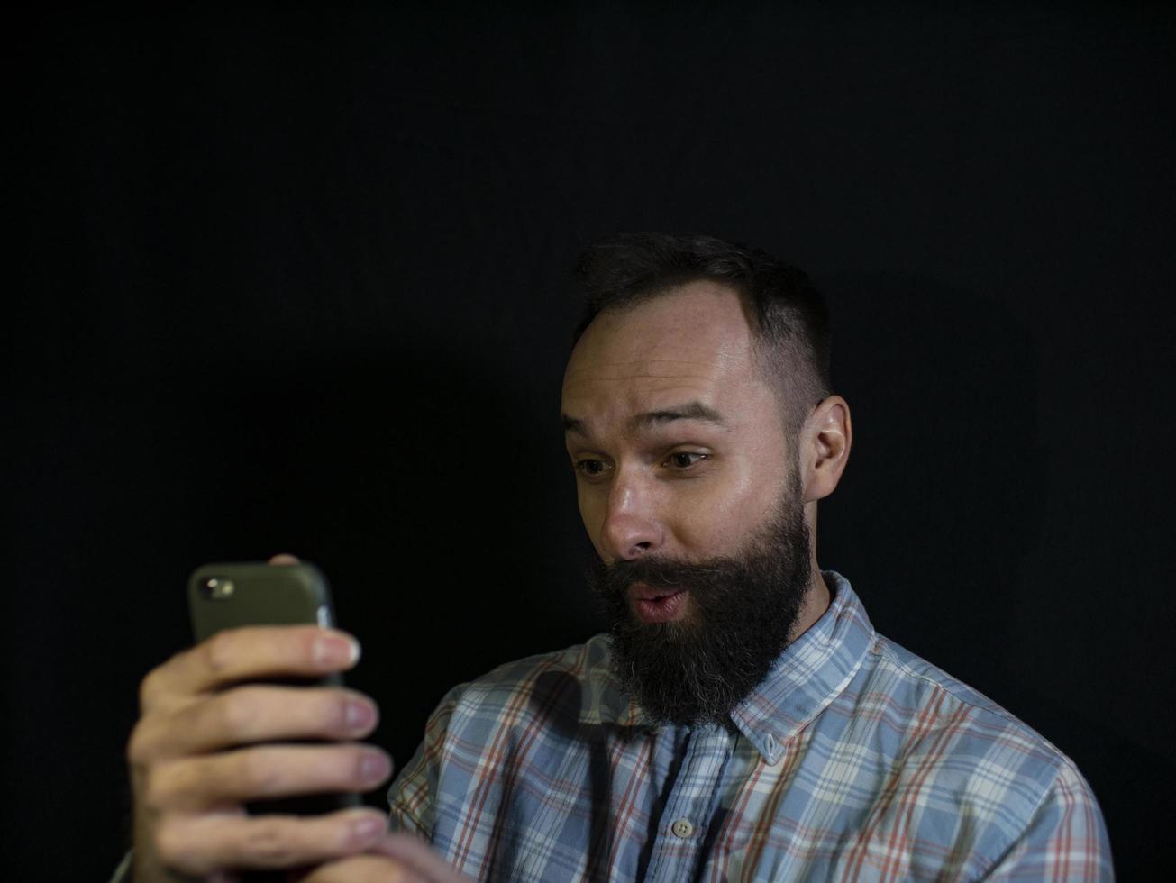 hombre con barba y bigote mira en un teléfono móvil foto