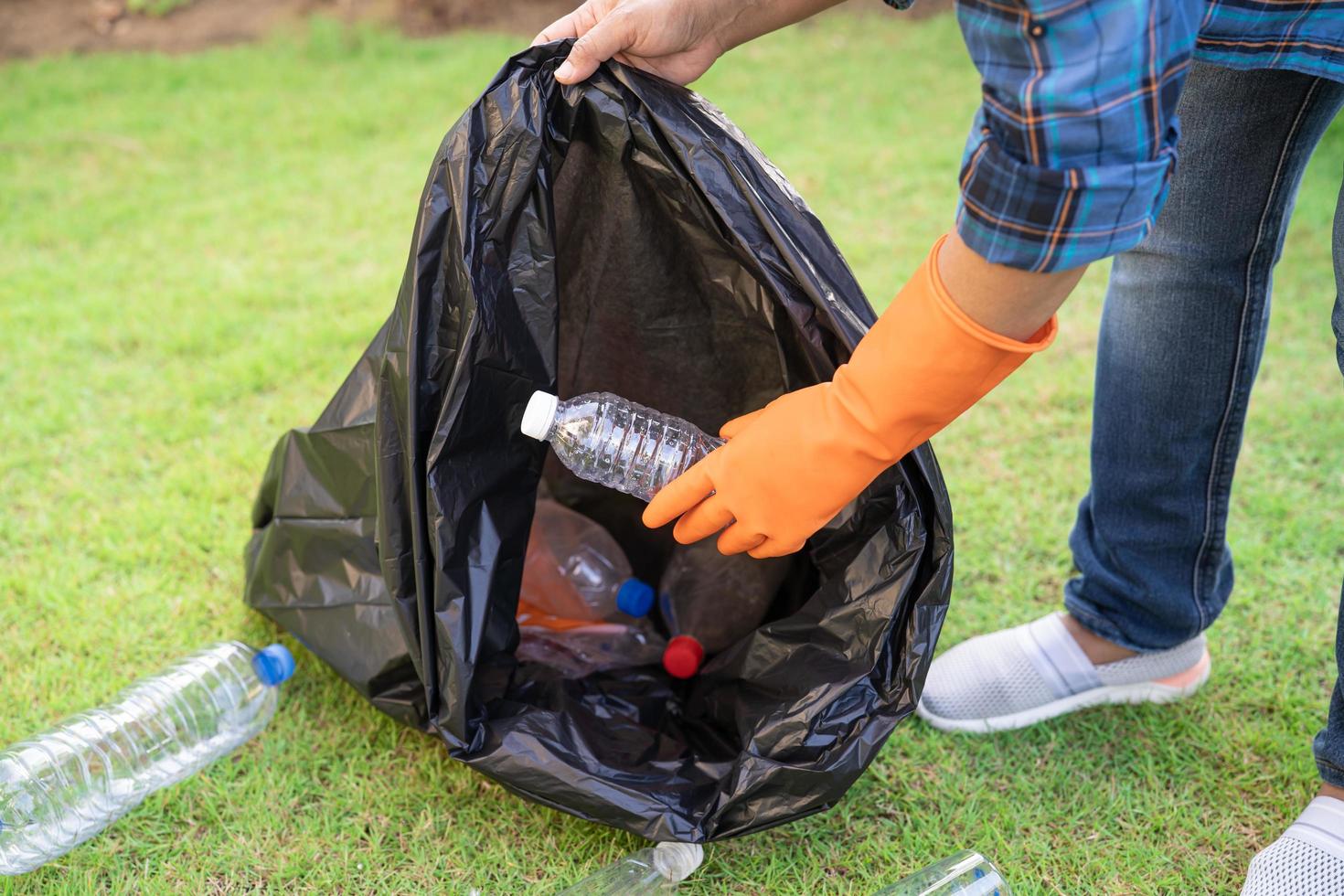 voluntario mujer asiática llevar botellas de plástico de agua en la bolsa de basura foto