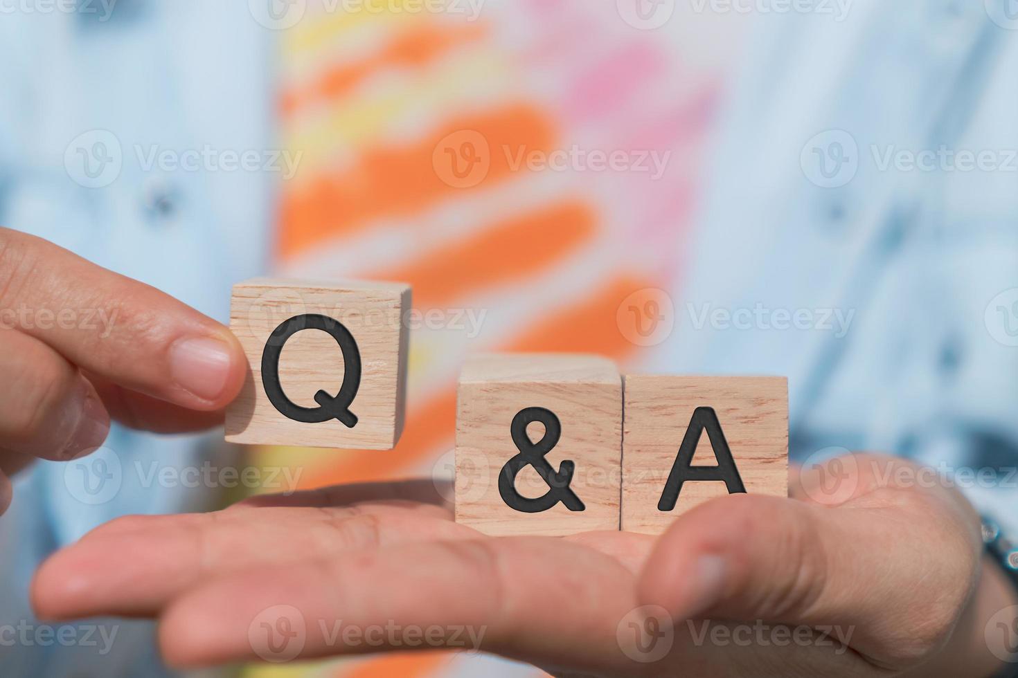 Q and A alphabet on wooden cube in hand hold with background photo
