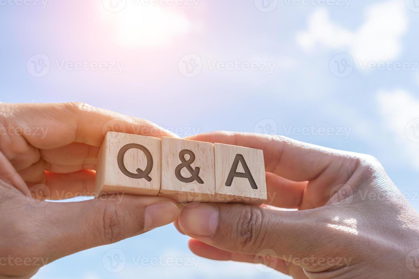 Q and A alphabet on wooden cube in hand hold with background photo