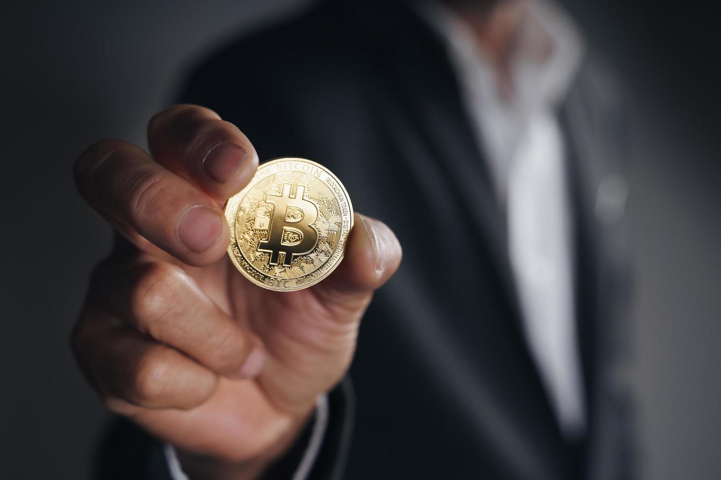 empresario sosteniendo un bitcoin dorado sobre fondo oscuro, criptomoneda foto