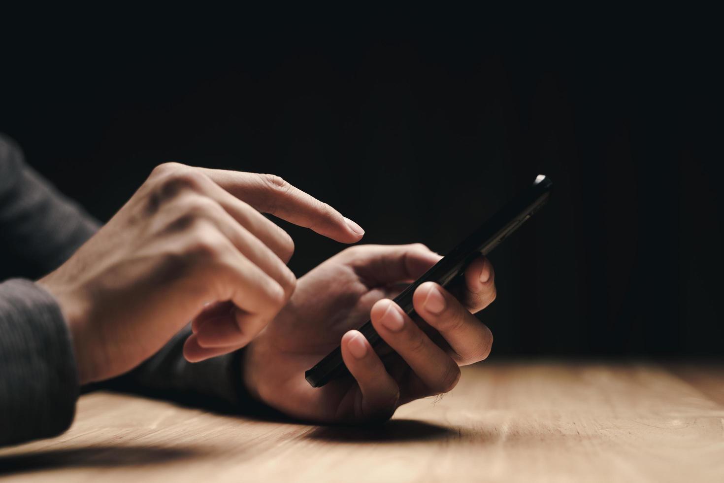 Hombre usando un teléfono inteligente en la mesa de madera, buscando, navegando foto