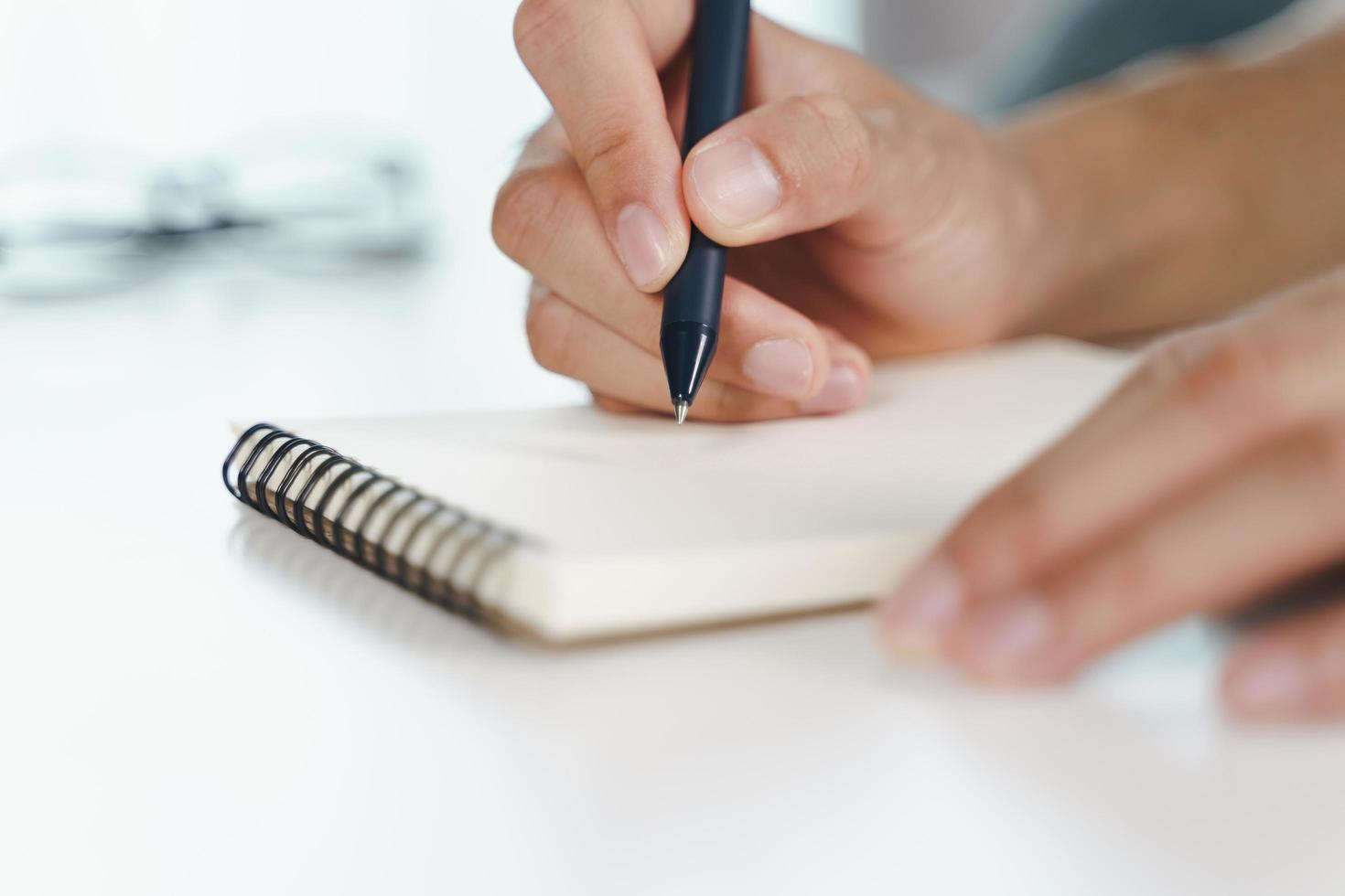 Las manos del hombre usan la pluma escribiendo en el bloc de notas sobre la mesa foto