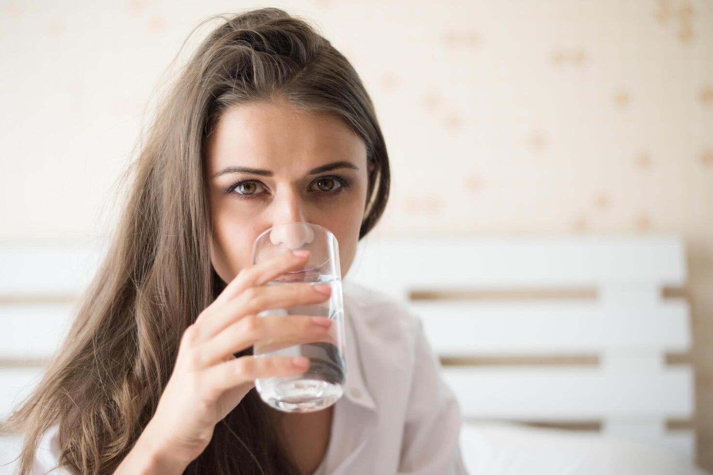 Bella mujer bebiendo agua dulce en la cama por la mañana foto