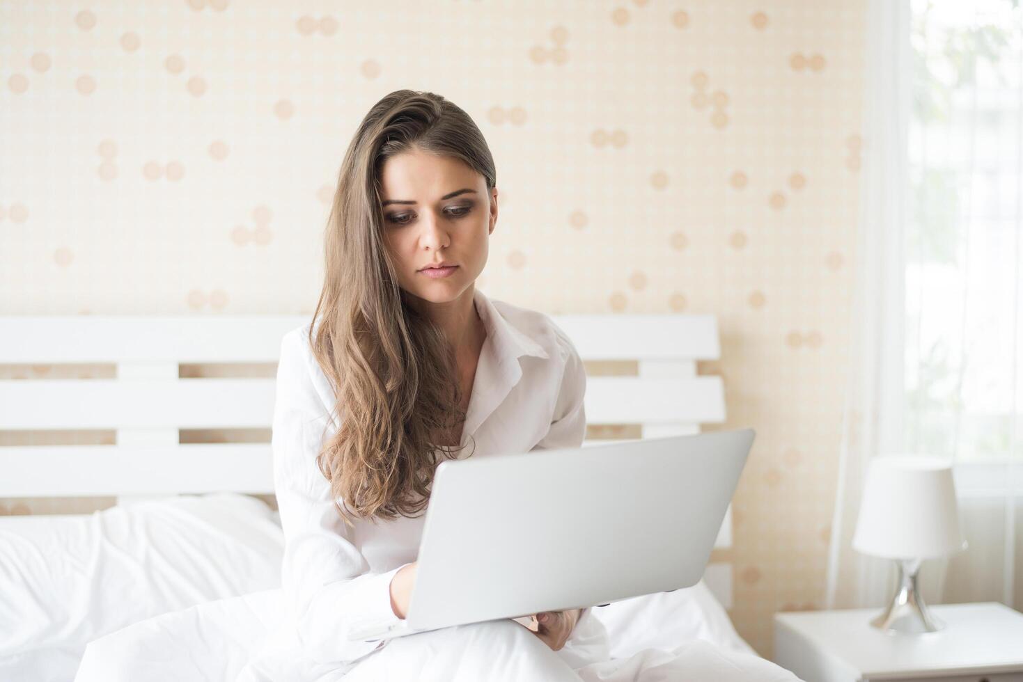 Feliz hermosa mujer trabajando en un portátil en la cama de la casa foto