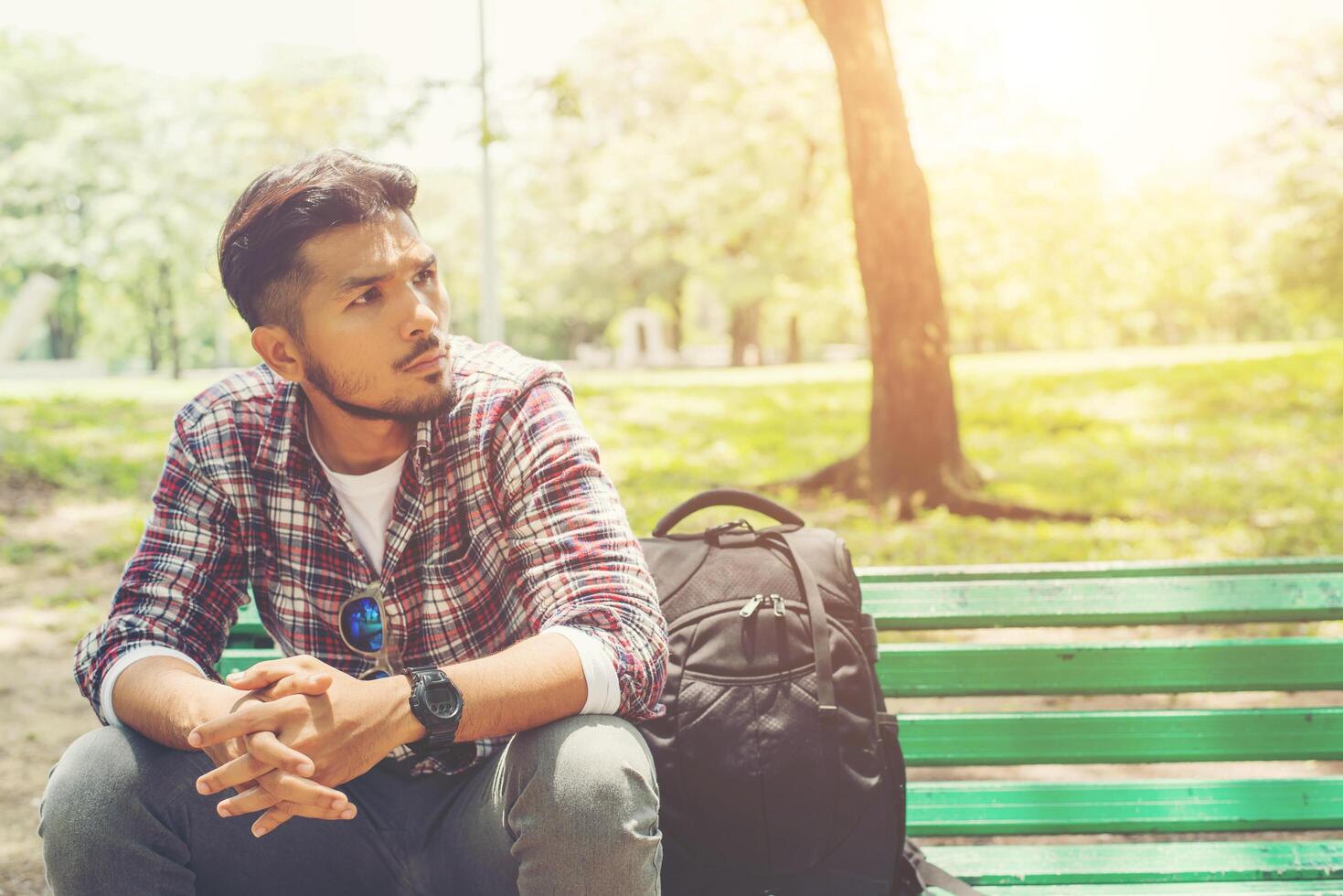 Young hipster man with backpack beside sitting on a wooden bench. photo