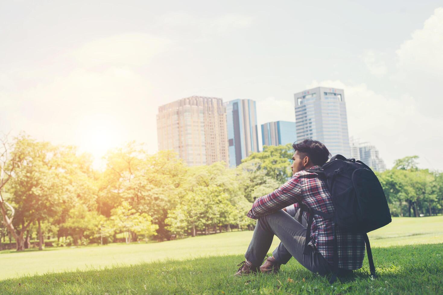 Rear view of relaxed young traveling man sitting on grass in the park. photo