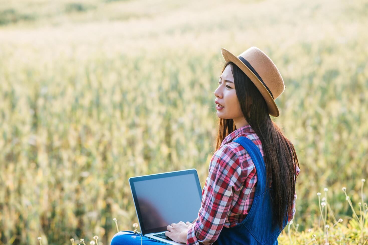 Smart woman farmer looking at barley field with laptop computer photo