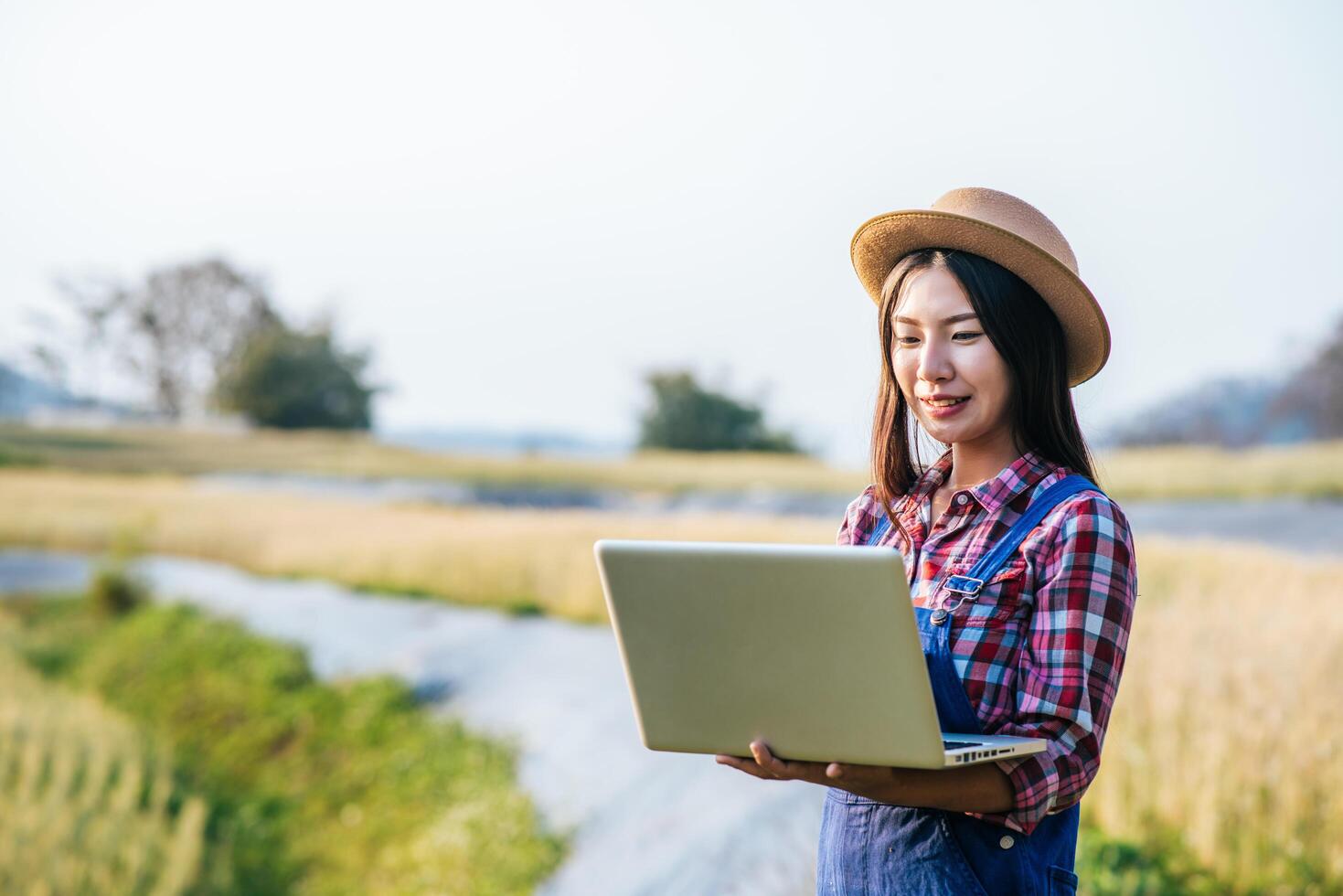 Mujer agricultora inteligente mirando campo de cebada con ordenador portátil foto
