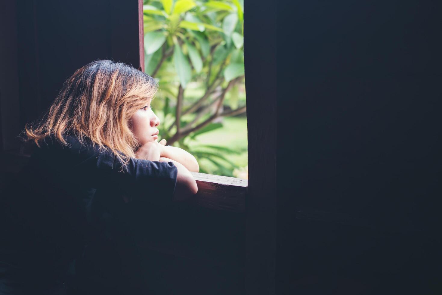 Young sad woman sitting on bench beside window photo