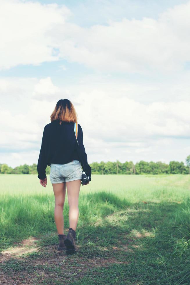 Back of young woman carrying retro camera in grass field photo