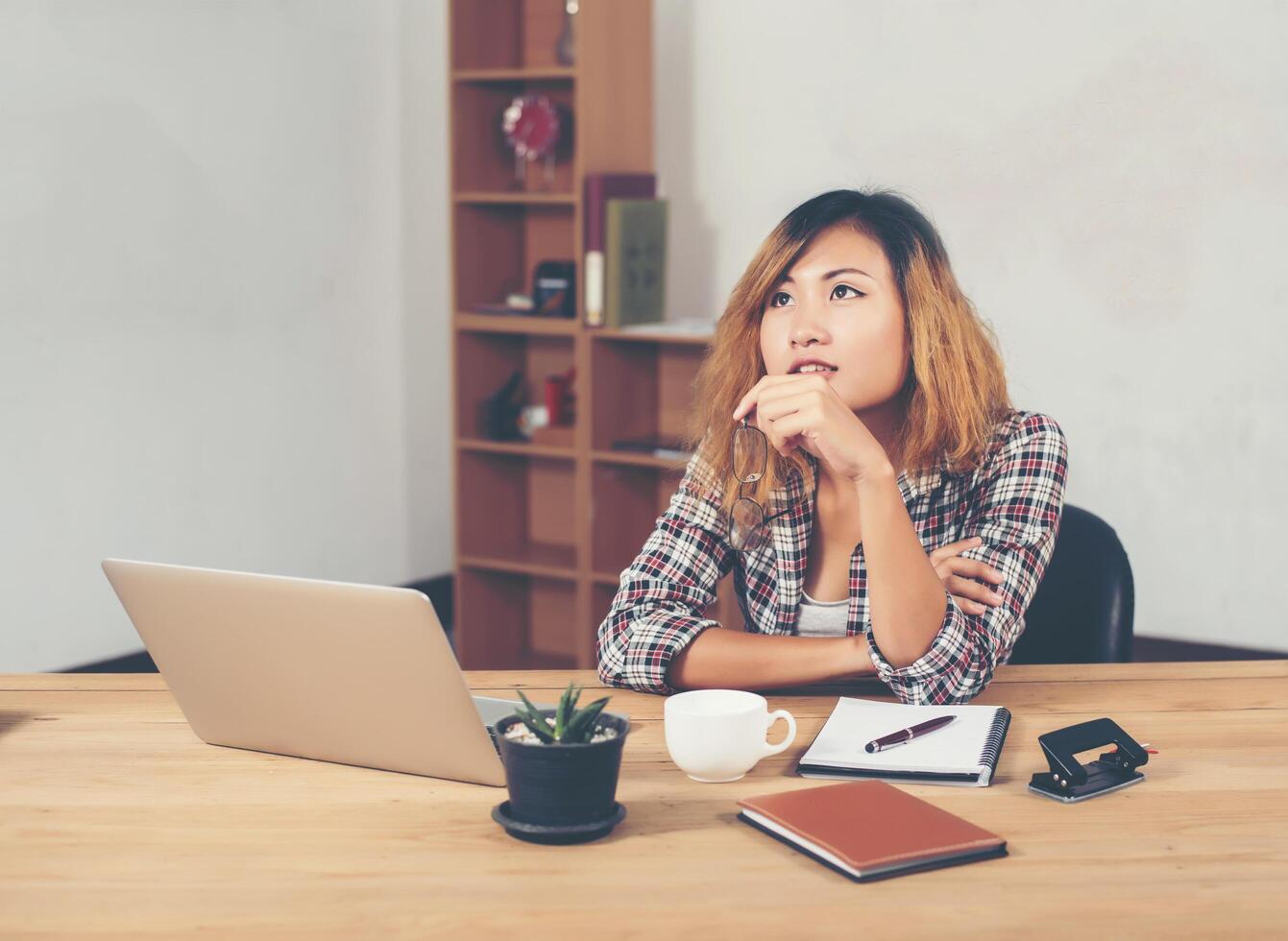 Young beautiful hipster woman sitting on workplace and thinking photo