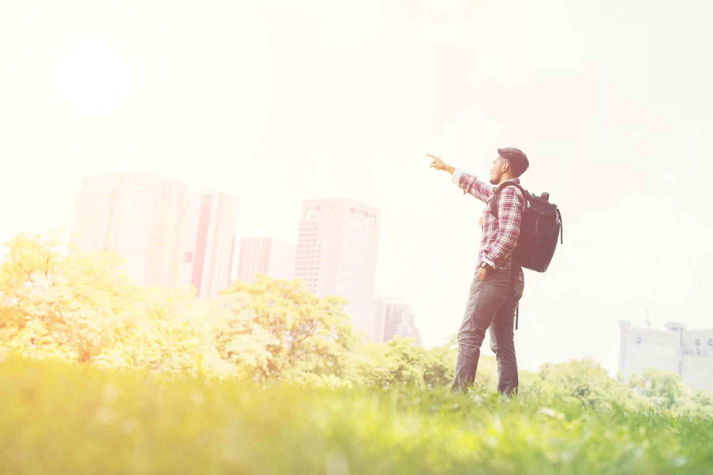 Young hipster man pointing to the town view from park while backpacking photo