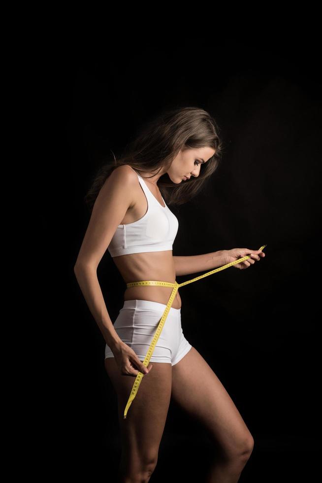 Beautiful young woman measuring her figure size with tape measure photo