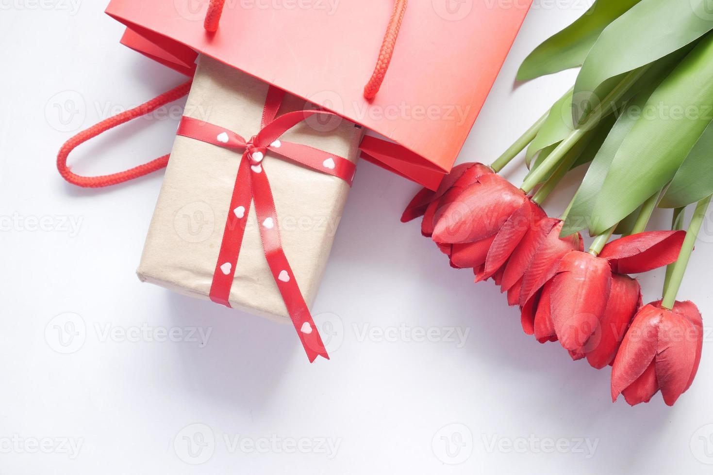 Caja de regalo en una bolsa de compras y flor de tulipán rojo en la mesa foto