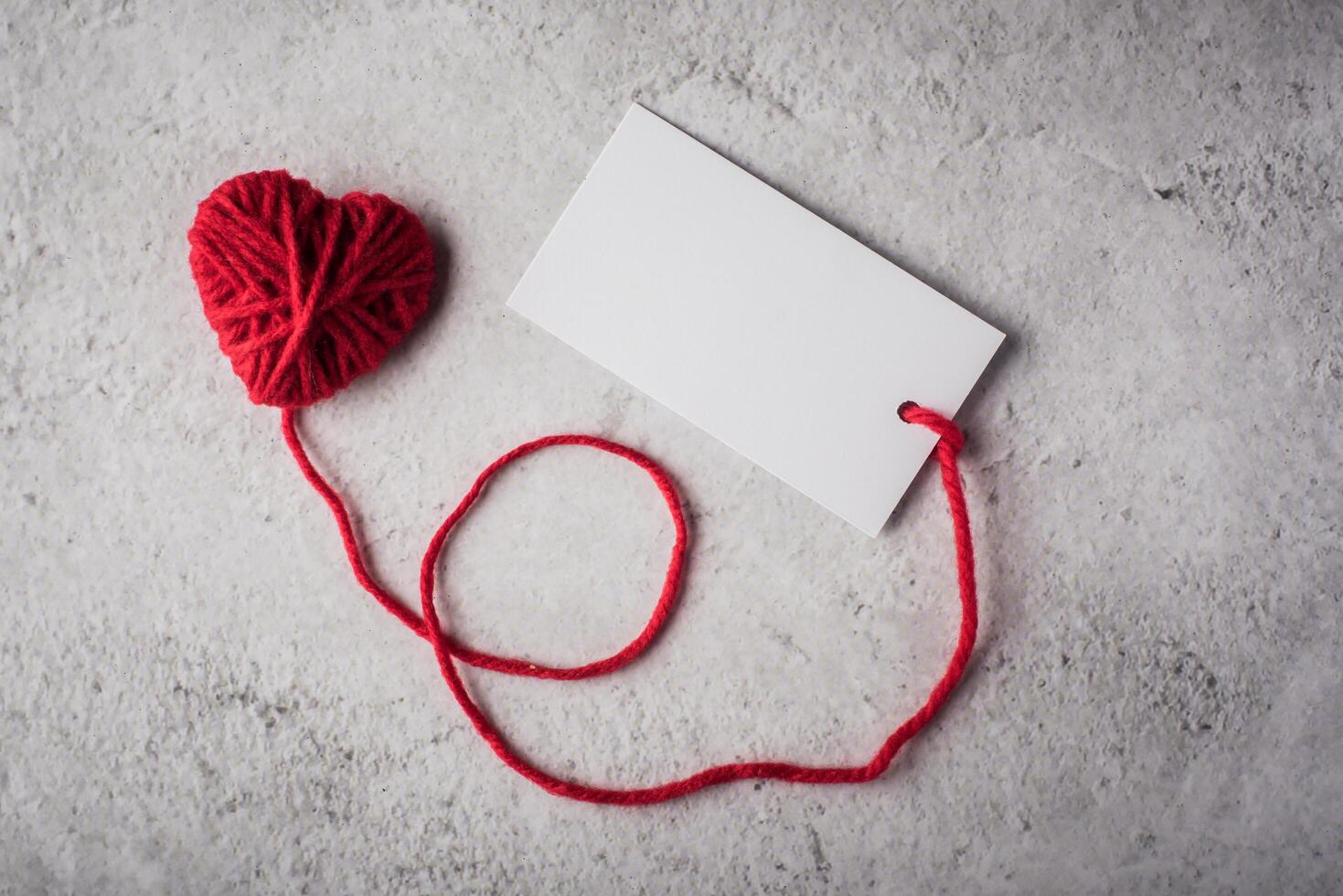 Red yarn heart shaped with white note card on the wall background photo