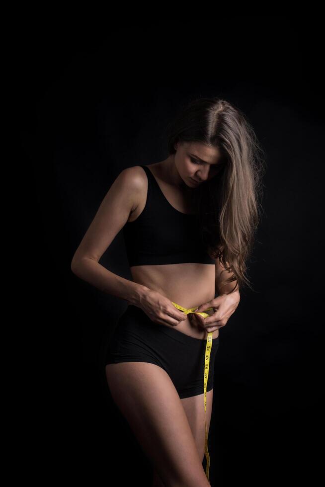 Retrato de una joven y bella mujer midiendo el tamaño de su figura con cinta métrica foto