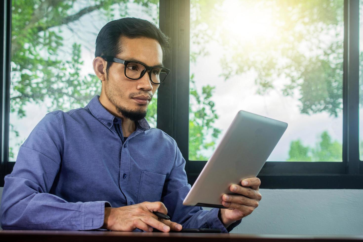 El hombre usa gafas leyendo el correo electrónico en la tableta, trabajo en casa foto