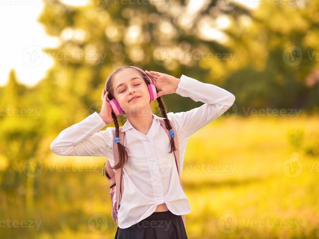 Beautiful little girl listening to music on headphones in autumn park photo