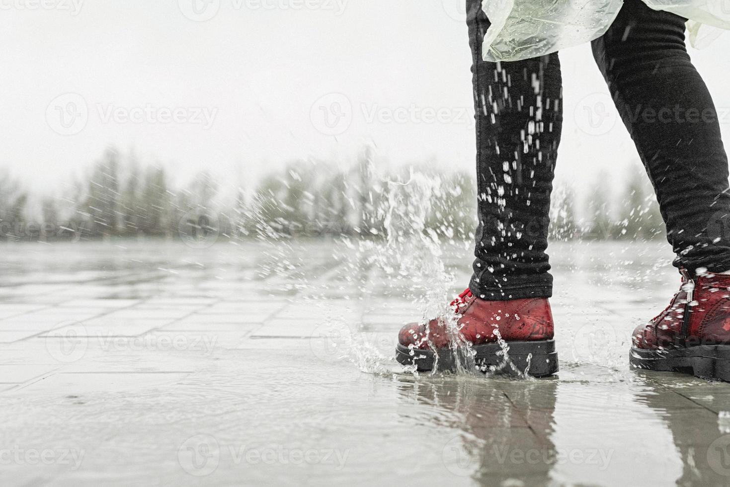 Piernas de mujer saltando en charcos con salpicaduras en día lluvioso foto