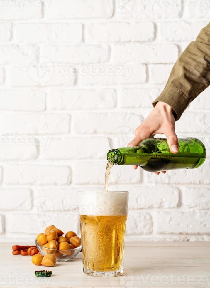 Cerveza vertiendo de botella en vidrio, fondo de pared de ladrillo blanco. foto