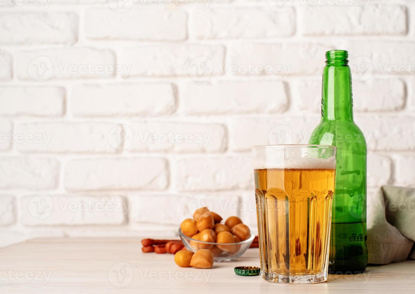 vaso lleno de cerveza, botella y bocadillos, fondo de pared de ladrillo blanco foto