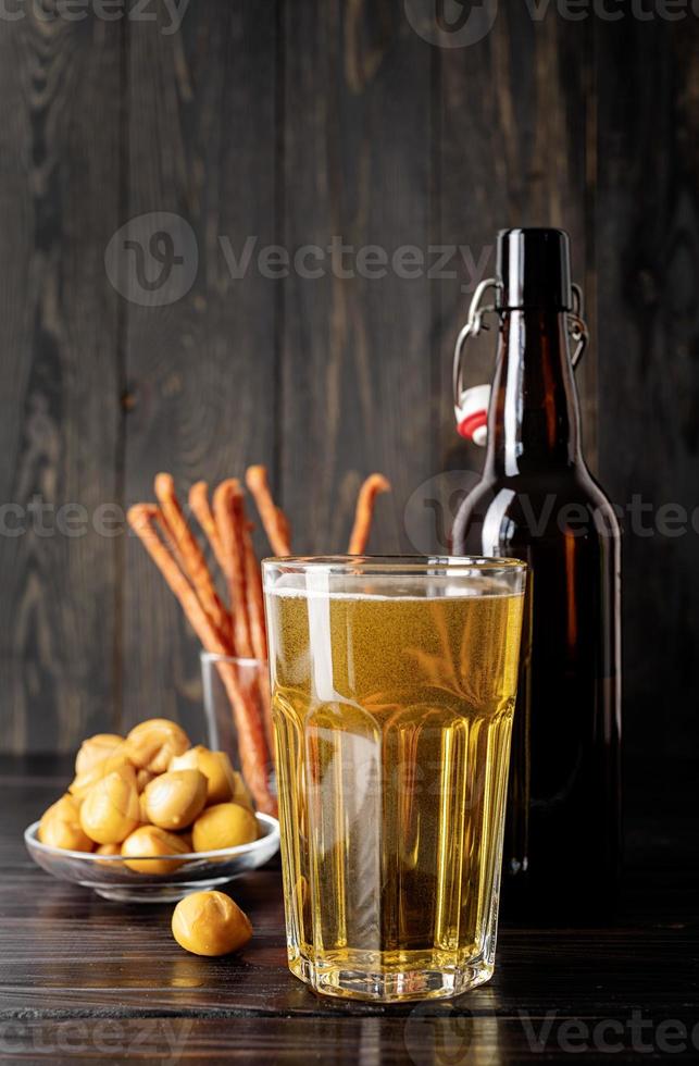 vaso lleno de cerveza, botella y bocadillos, fondo de madera negra foto