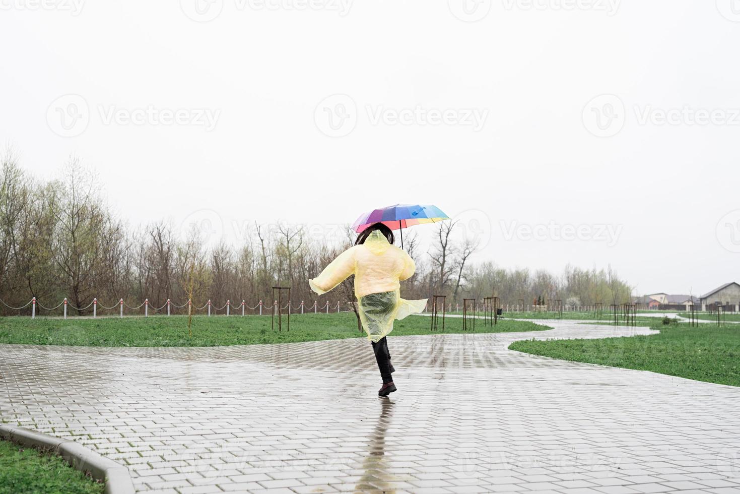 Mujer sosteniendo coloridos paraguas caminando bajo la lluvia, vista desde atrás foto