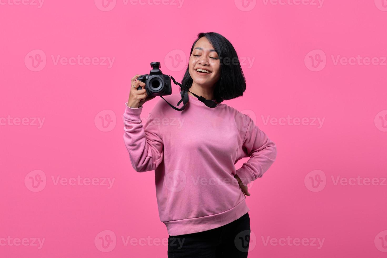 Happy smiling young woman holding camera on pink background photo