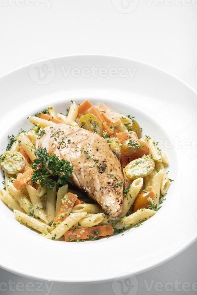 Pechuga de pollo frito con penne y verduras salteadas plato de pasta sobre fondo blanco. foto