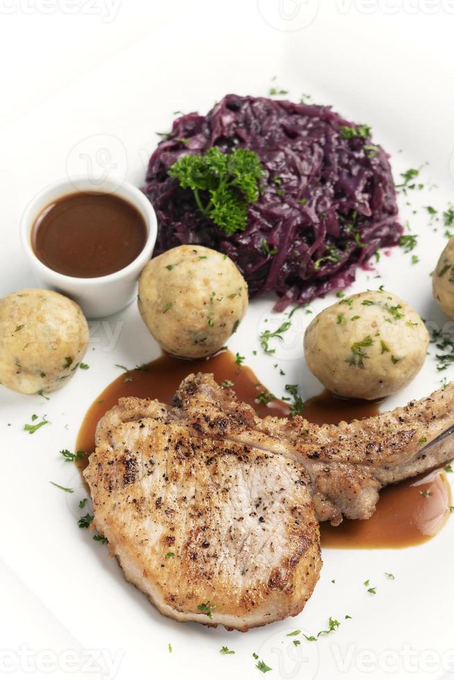 Chuleta de cerdo a la parrilla al estilo alemán con albóndigas de pan y comida tradicional de col lombarda sobre fondo blanco. foto