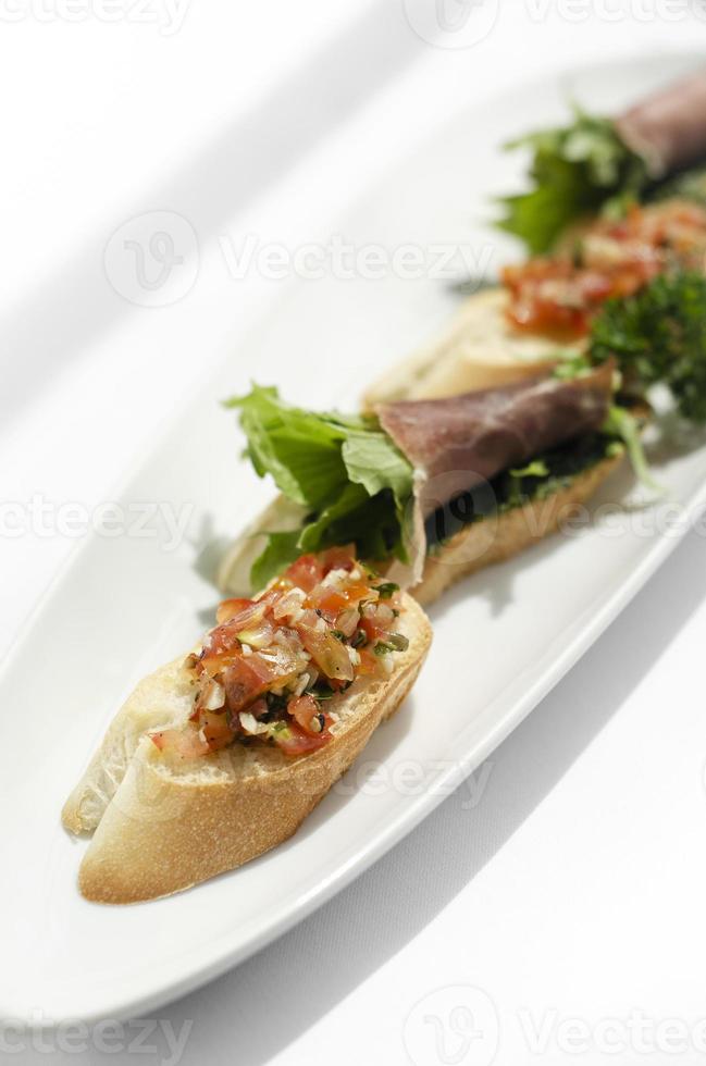 Mixed tapas plate with tomato bruschetta and serrano cured ham on white plate photo