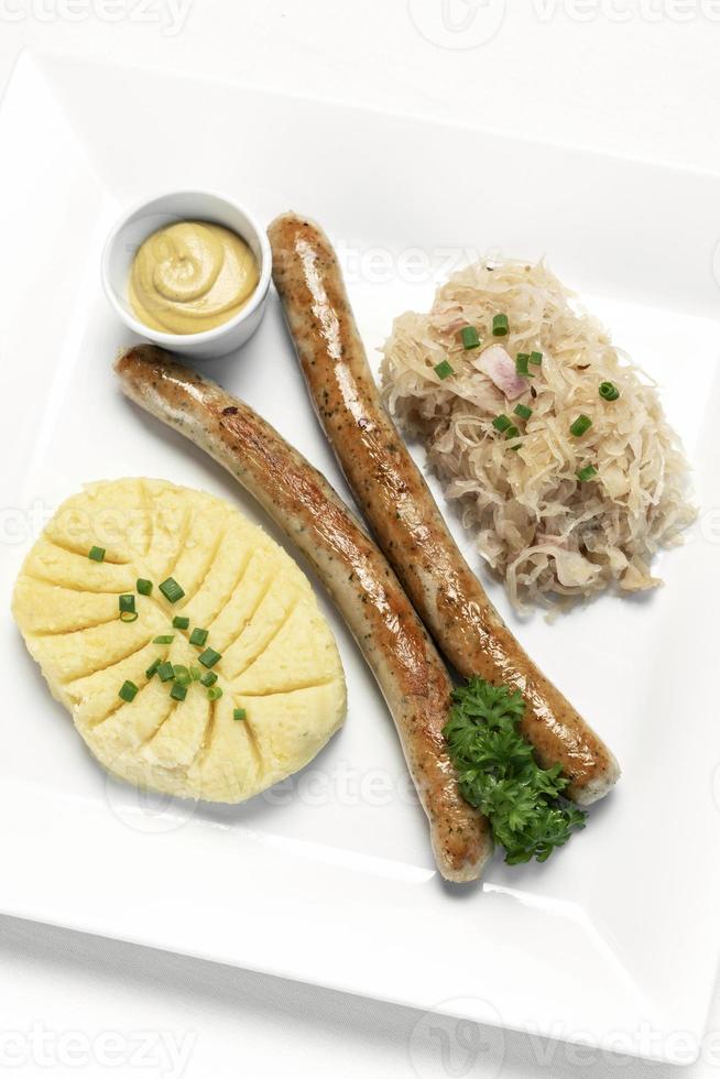 Salchicha Thuringer alemán con puré de patatas y chucrut comida en la placa blanca. foto