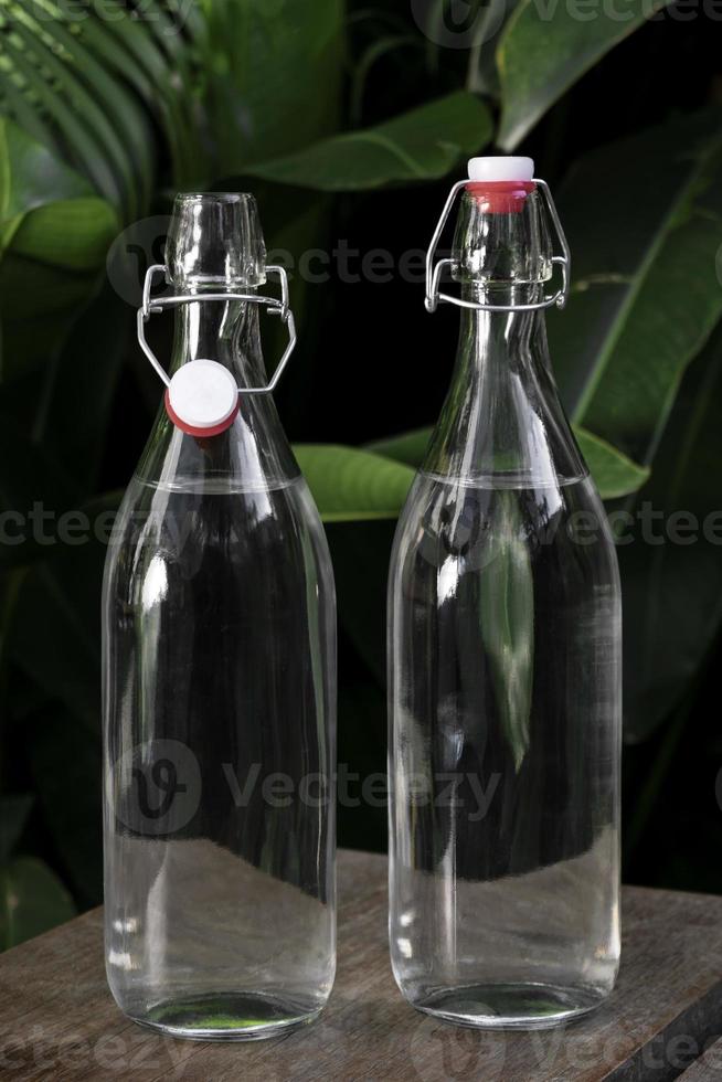 Botella de agua con tapa abatible de vidrio blanco transparente al aire libre en una mesa de jardín foto