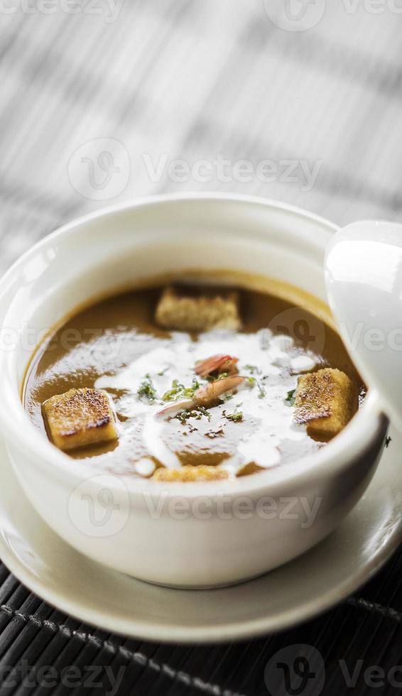 Tazón de sopa de crema de mariscos con camarones y gambas con picatostes en la mesa foto