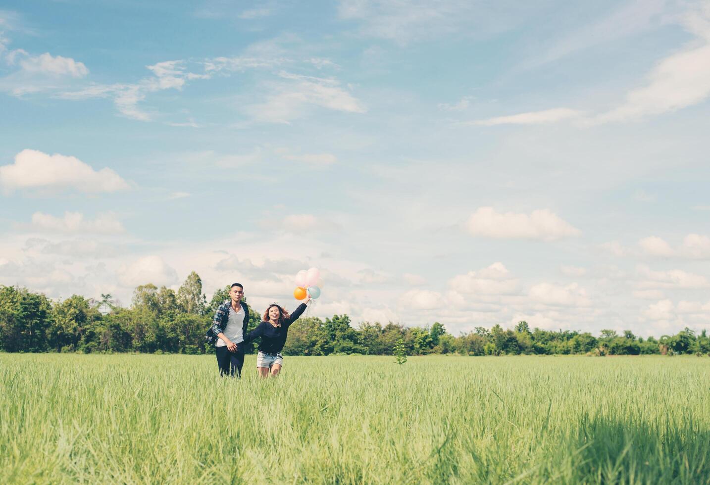 Young Couple running and holding balloon in the green grass below photo