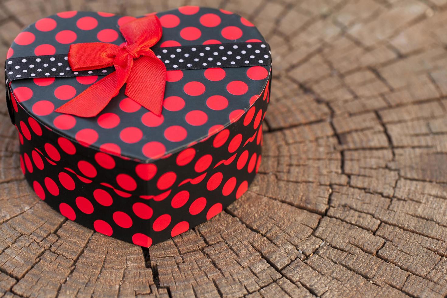 Caja de regalo en forma de corazón sobre tronco de madera foto